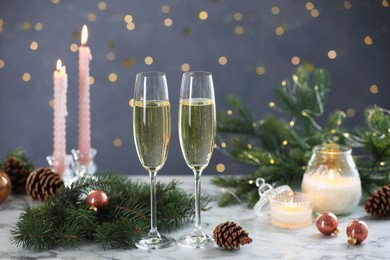 Photo of Delicious champagne in glasses and Christmas decor on marble table against blurred lights