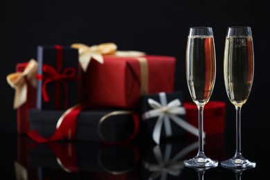 Photo of Delicious champagne in glasses and Christmas presents on black mirror surface, closeup. Space for text