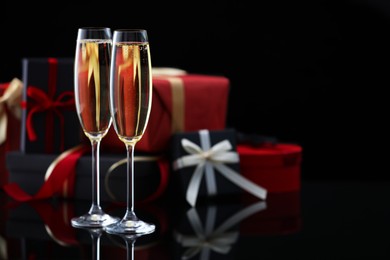 Photo of Delicious champagne in glasses and Christmas presents on black mirror surface, closeup. Space for text