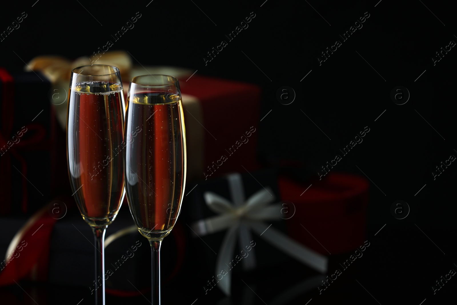 Photo of Delicious champagne in glasses and Christmas presents on black background, closeup. Space for text