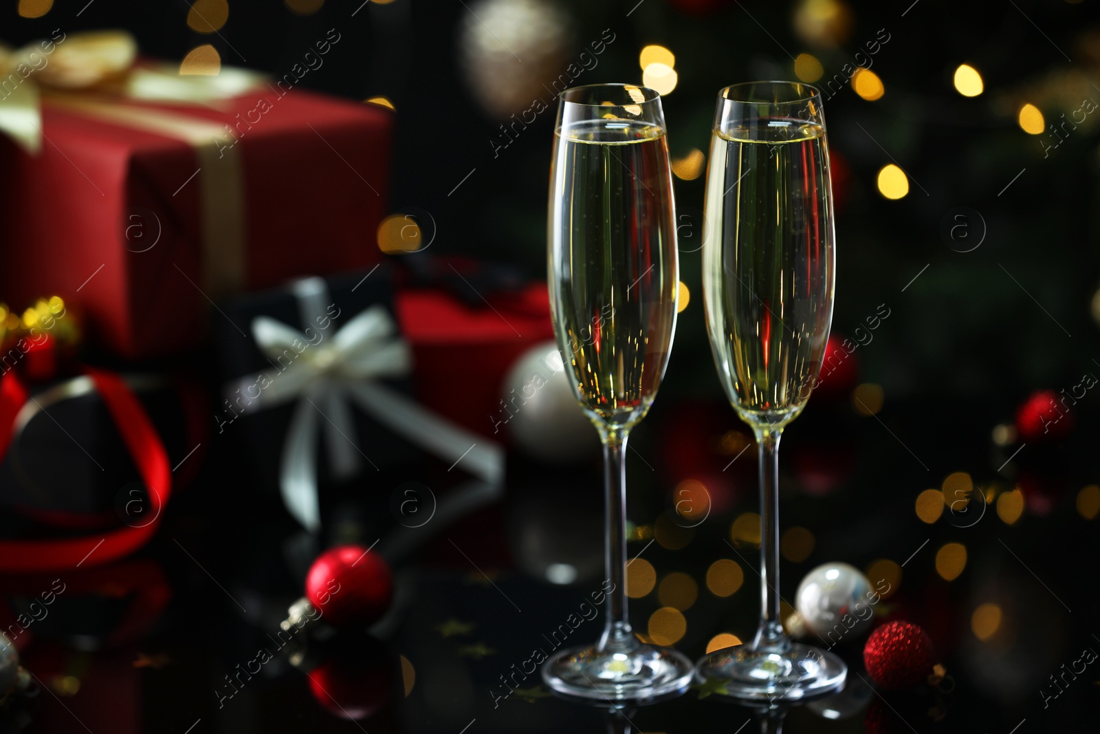 Photo of Delicious champagne in glasses and Christmas decor on black mirror surface against blurred lights, closeup. Space for text