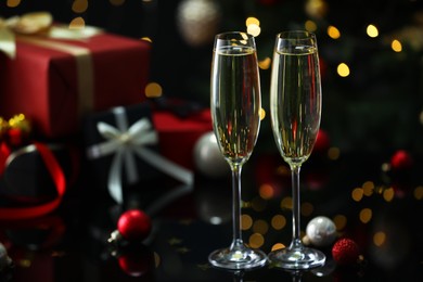 Photo of Delicious champagne in glasses and Christmas decor on black mirror surface against blurred lights, closeup. Space for text