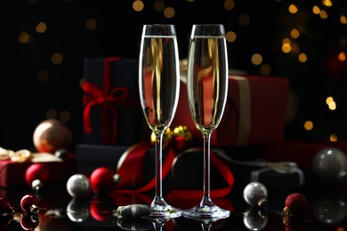 Photo of Delicious champagne in glasses and Christmas decor on black mirror surface against blurred lights, closeup