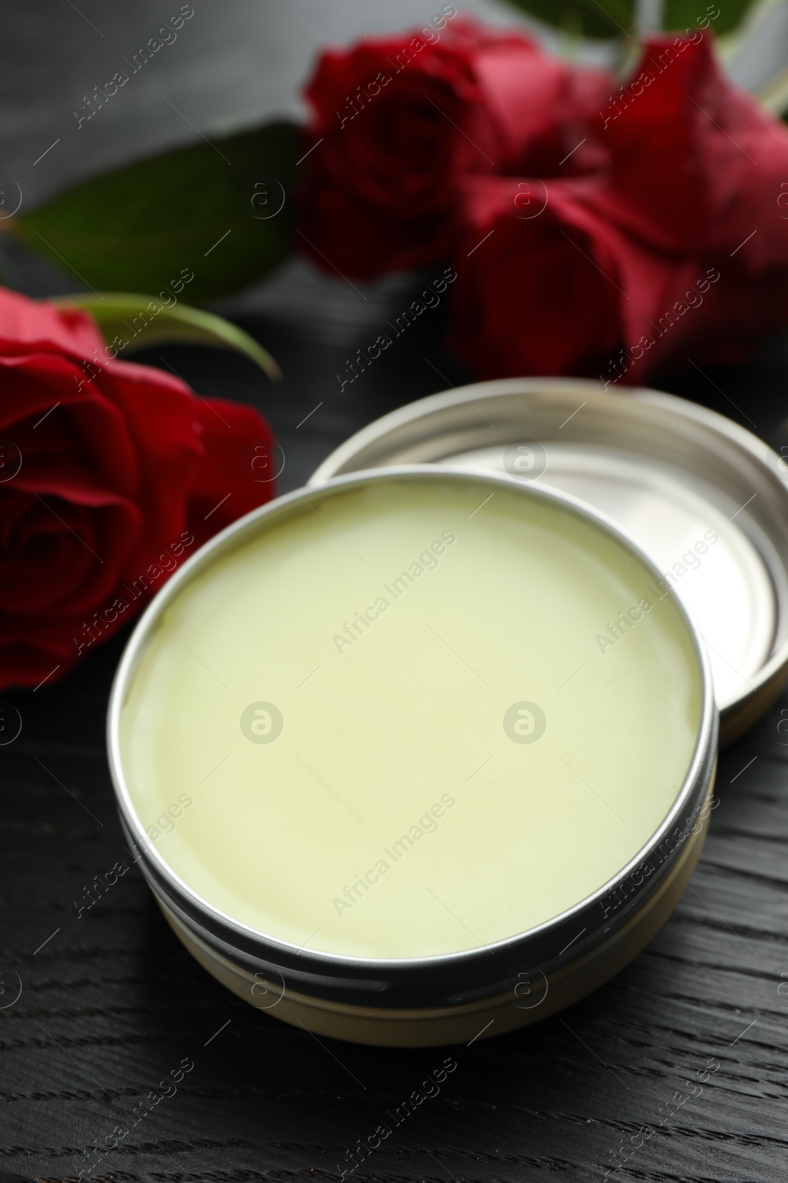 Photo of Natural solid perfume and roses on black wooden table, closeup