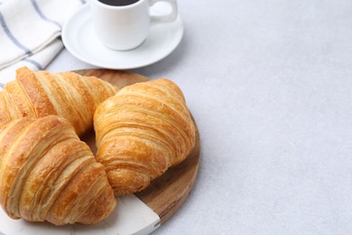 Photo of Tasty fresh croissants and cup of coffee on light table, closeup. Space for text