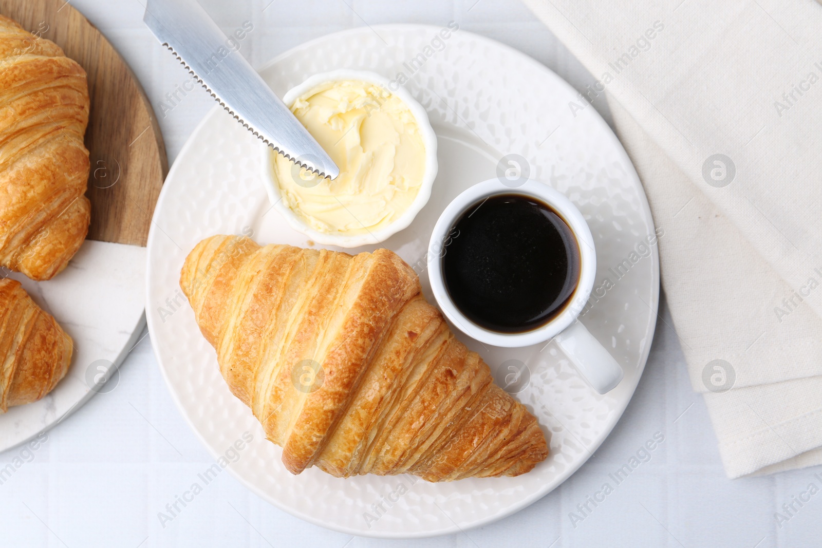 Photo of Tasty fresh croissants served with butter and cup of coffee on white tiled table, flat lay