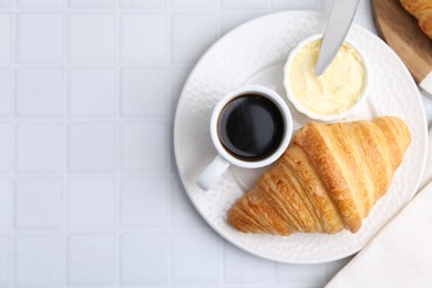 Photo of Tasty fresh croissant served with butter and cup of coffee on white tiled table, top view. Space for text