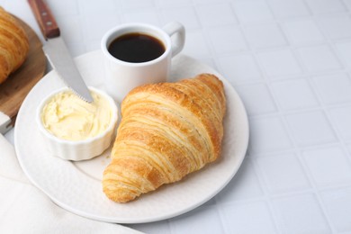 Photo of Tasty fresh croissant served with butter and cup of coffee on white tiled table, space for text