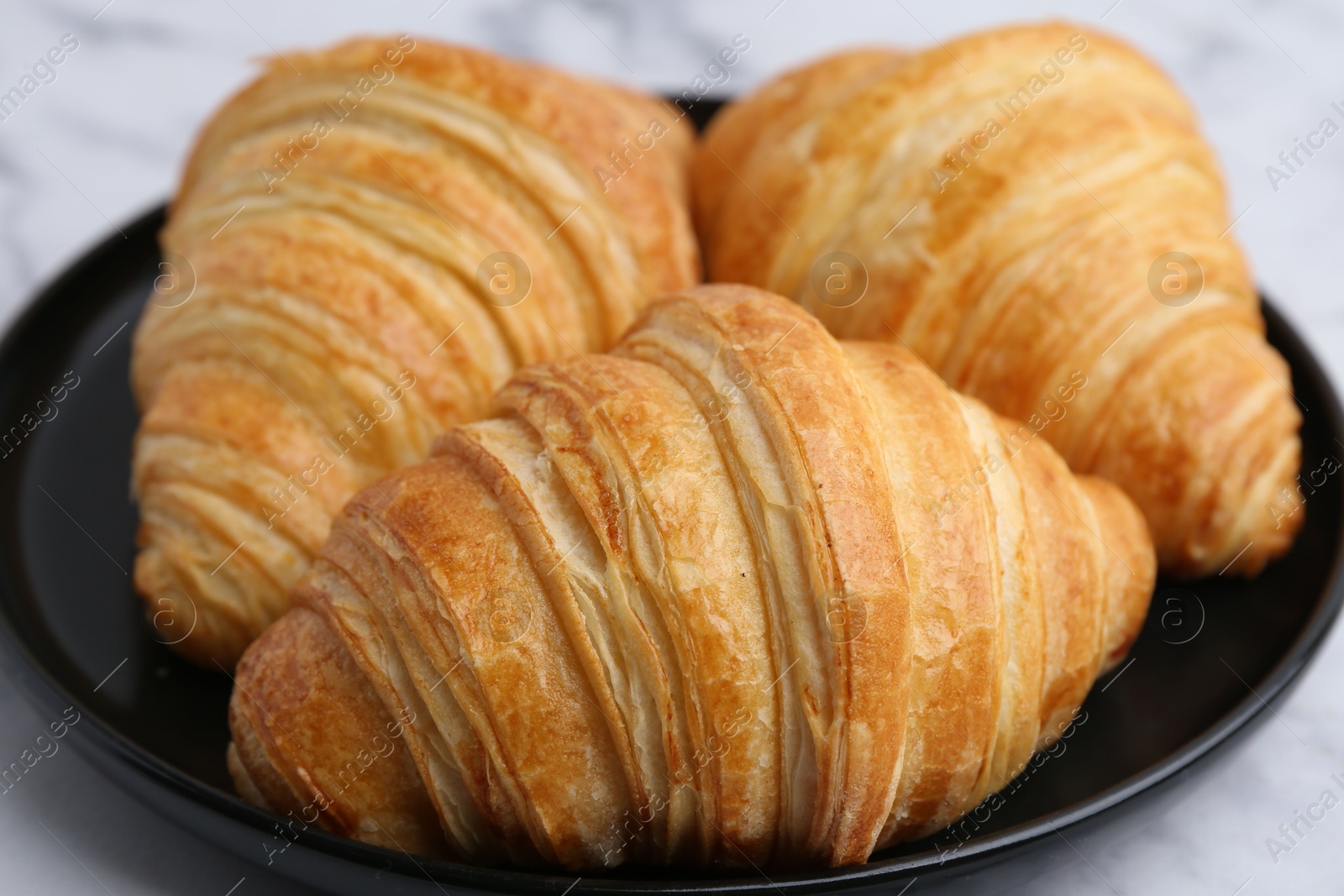 Photo of Tasty fresh croissants on white marble table, closeup. Puff pastry