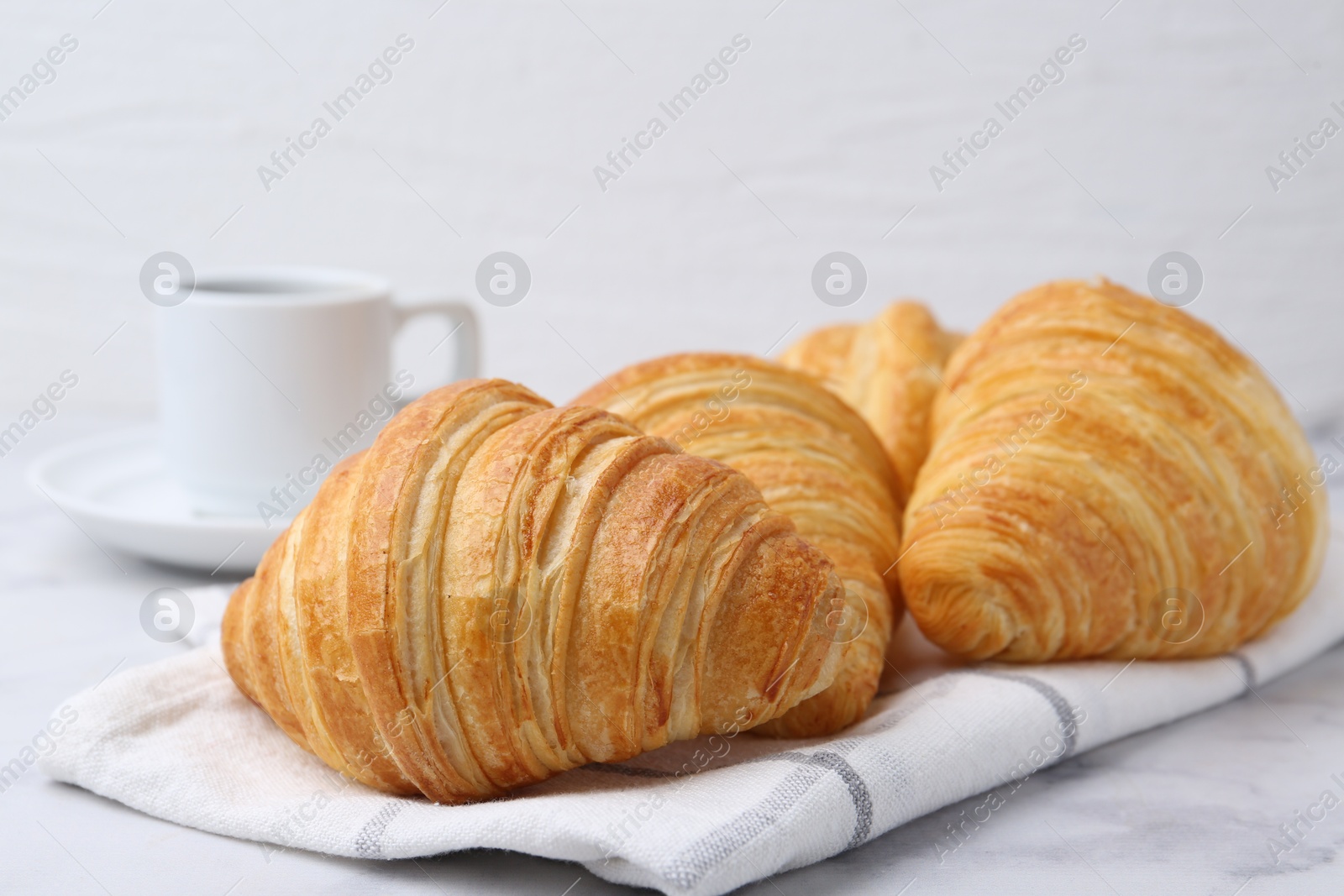 Photo of Tasty fresh croissants and cup of drink on white marble table, closeup