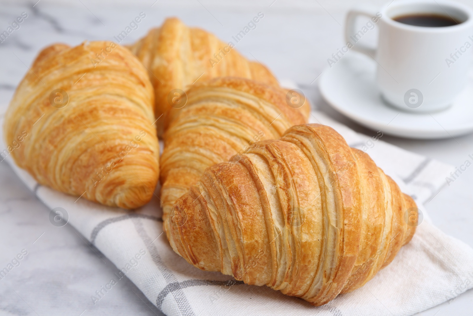 Photo of Tasty fresh croissants and cup of coffee on white marble table, closeup