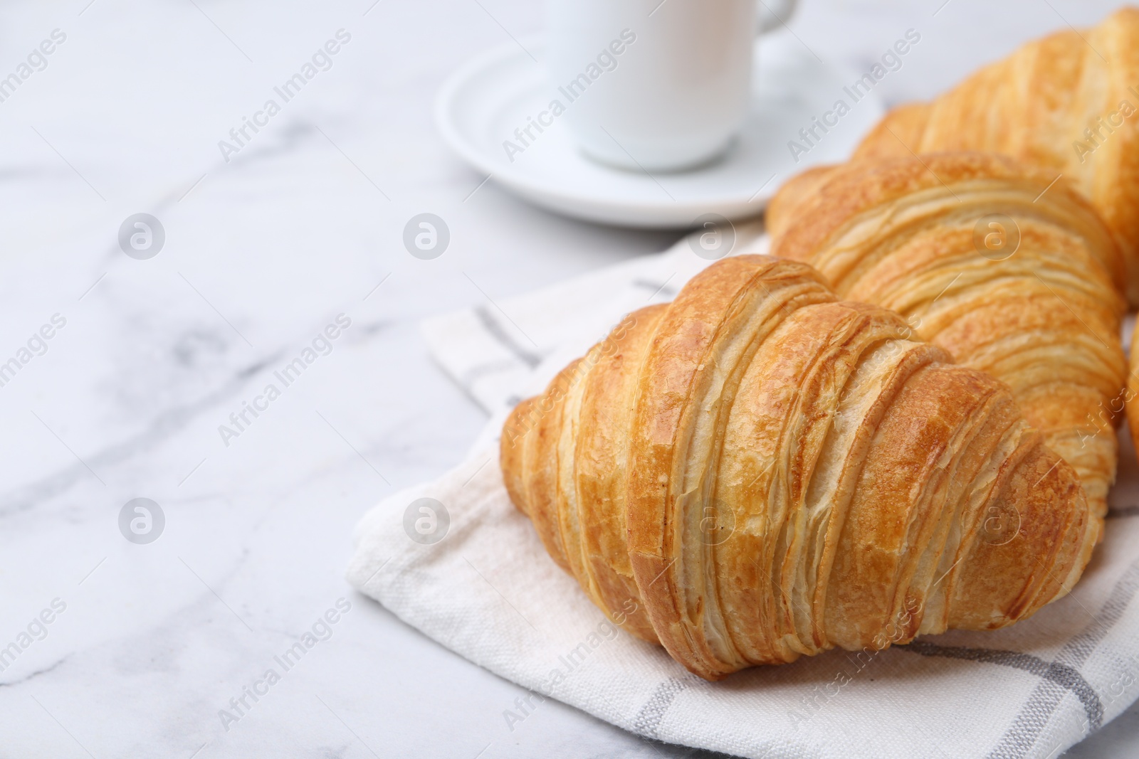 Photo of Tasty fresh croissants on white marble table, closeup. Space for text