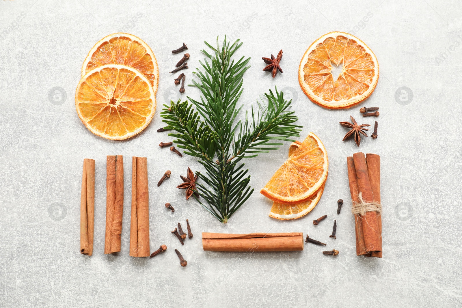 Photo of Different spices, dried orange slices and fir tree branches on light grey table, flat lay. Christmas season