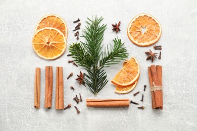 Photo of Different spices, dried orange slices and fir tree branches on light grey table, flat lay. Christmas season