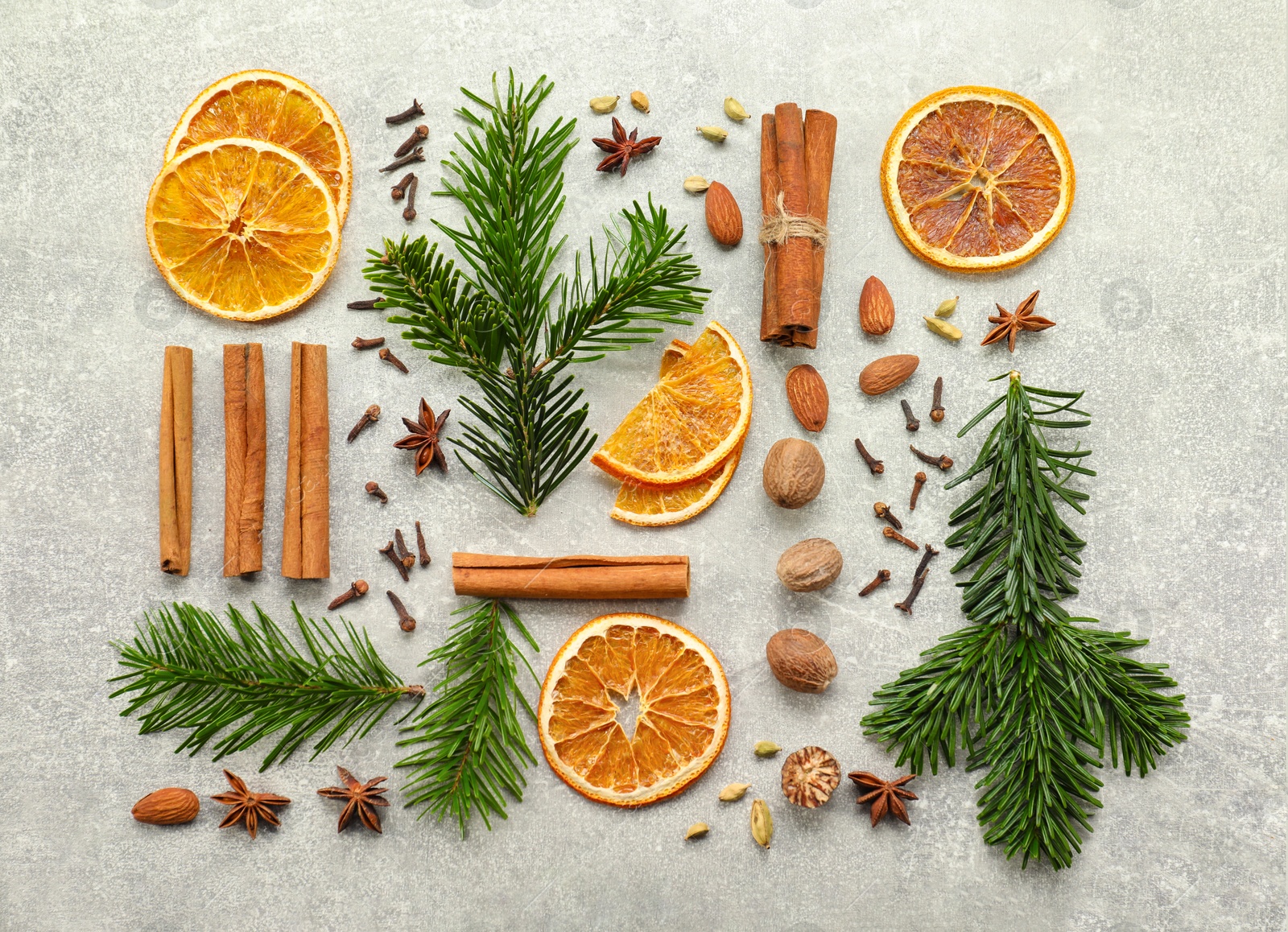 Photo of Different spices, dried orange slices and fir tree branches on light grey table, flat lay. Christmas season