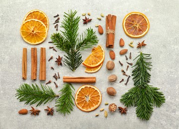 Photo of Different spices, dried orange slices and fir tree branches on light grey table, flat lay. Christmas season