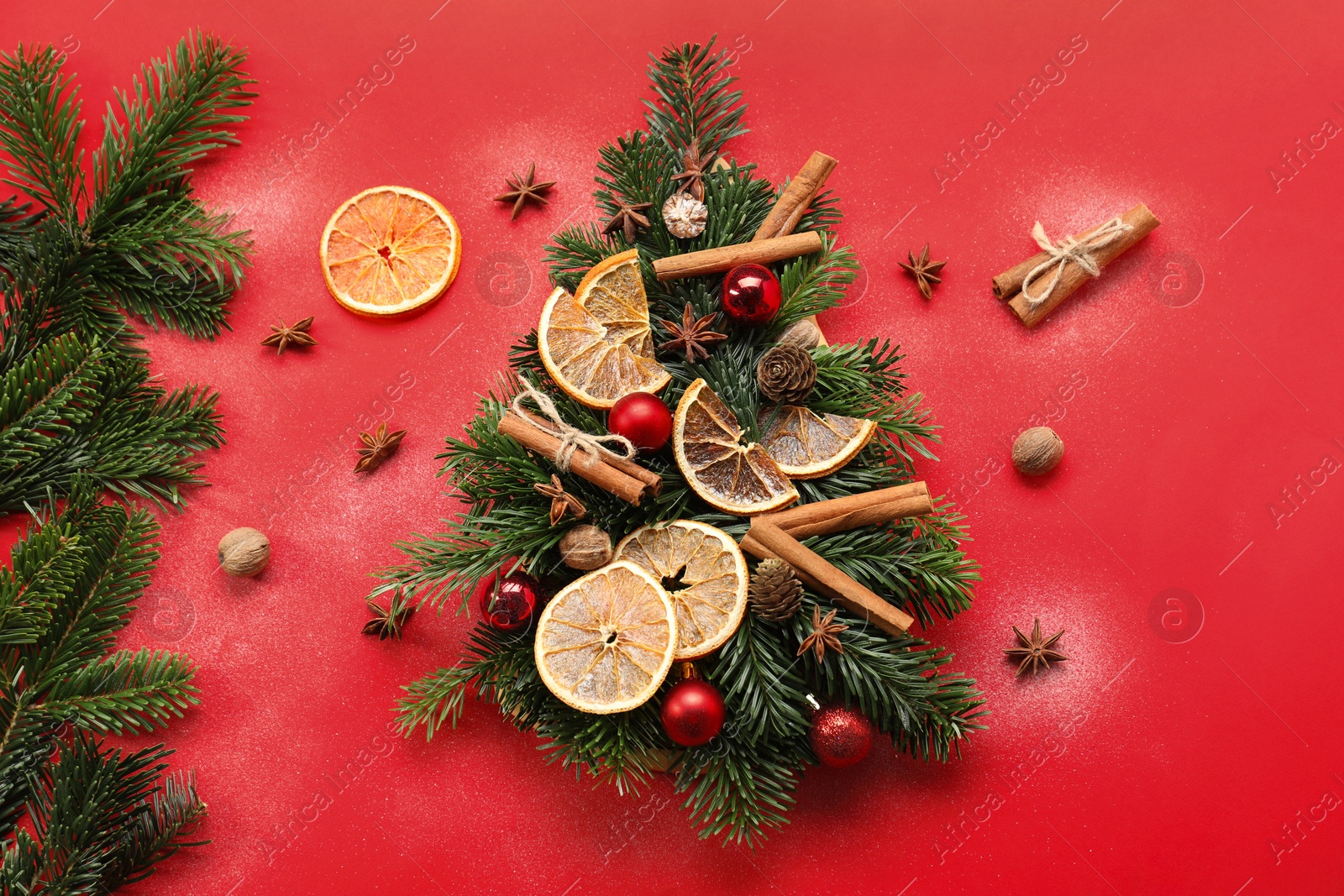 Photo of Christmas tree made of fir branches, baubles and different spices on red background, flat lay