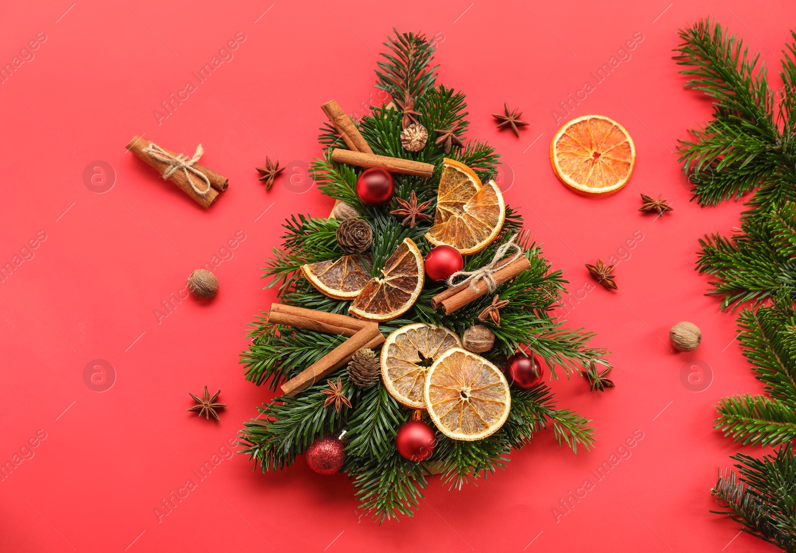 Photo of Christmas tree made of fir branches, baubles and different spices on red background, flat lay