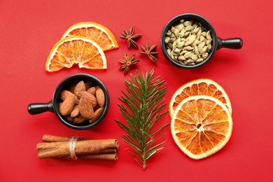 Photo of Different spices, dried orange slices and fir tree branch on red background, flat lay. Christmas season