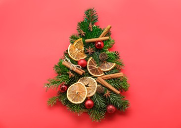 Photo of Christmas tree made of fir branches, baubles and different spices on red background, flat lay