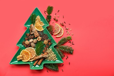 Photo of Different spices, dried orange slices and fir tree branches on red background, flat lay with space for text. Christmas season