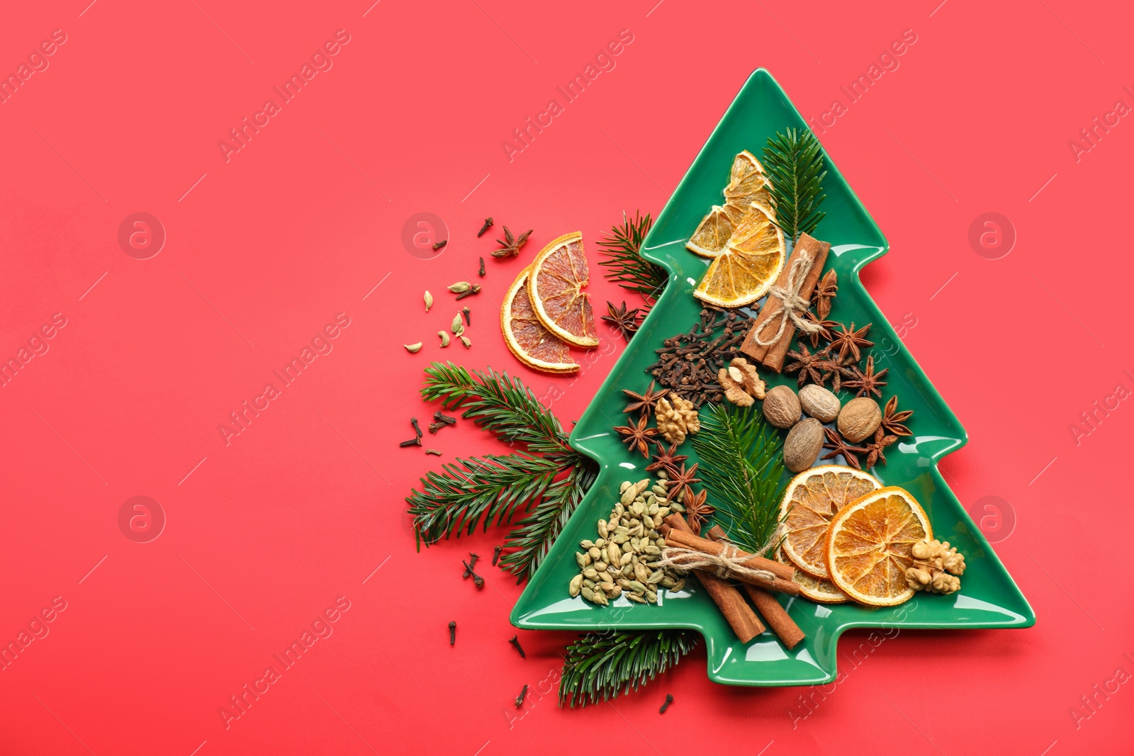 Photo of Different spices, dried orange slices and fir tree branches on red background, flat lay with space for text. Christmas season