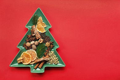 Photo of Different spices, dried orange slices and fir tree branches on red background, flat lay with space for text. Christmas season