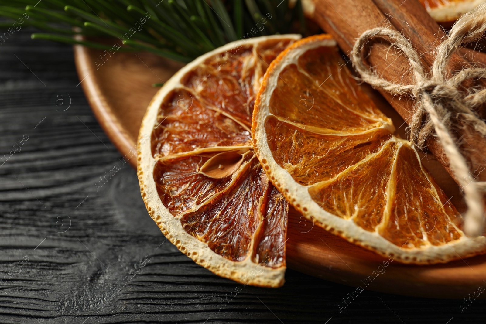 Photo of Different spices, dried orange slices and fir tree branches on black wooden table, closeup. Christmas season