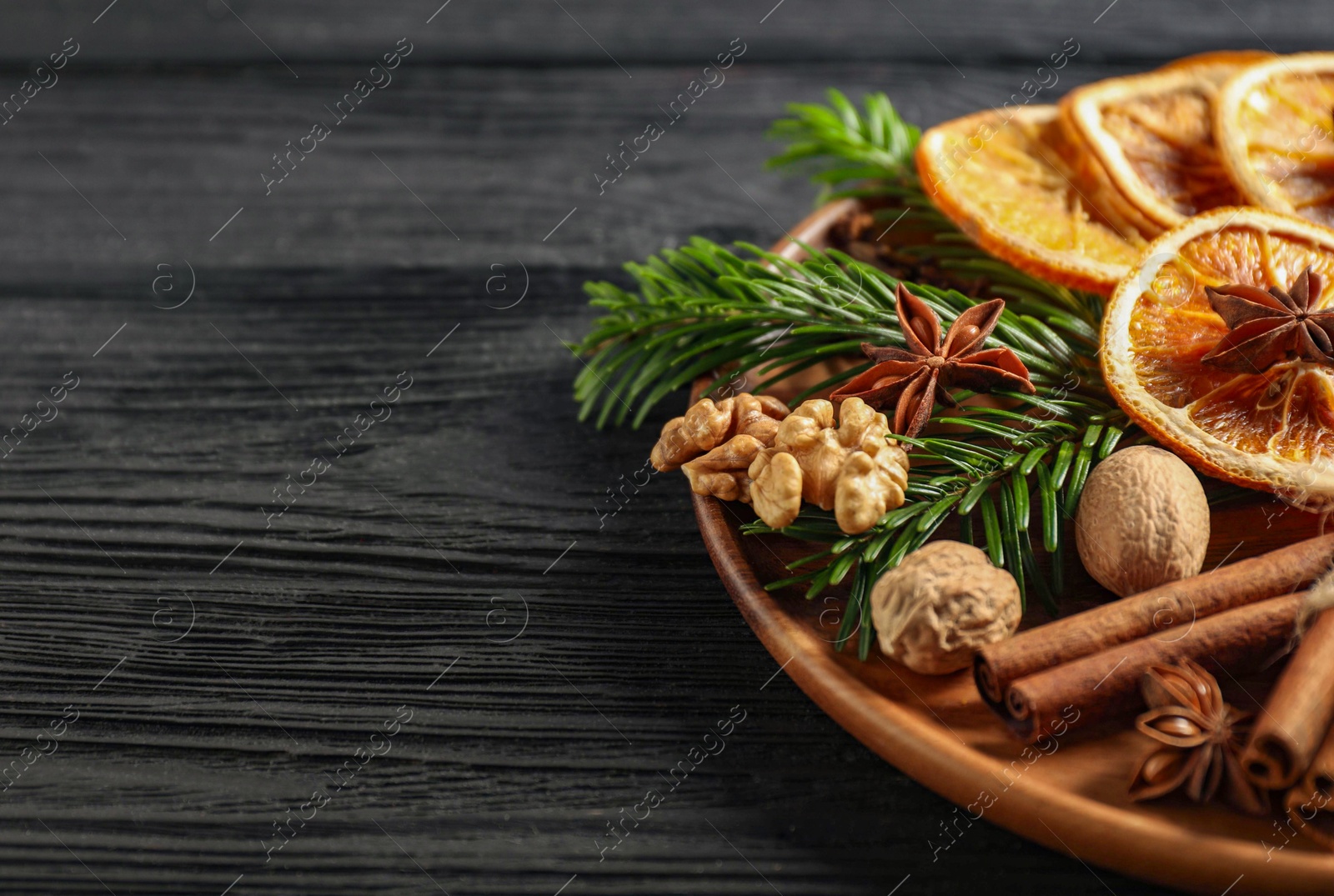 Photo of Different spices, dried orange slices and fir tree branches on black wooden table, closeup with space for text. Christmas season