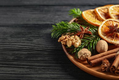 Photo of Different spices, dried orange slices and fir tree branches on black wooden table, closeup with space for text. Christmas season