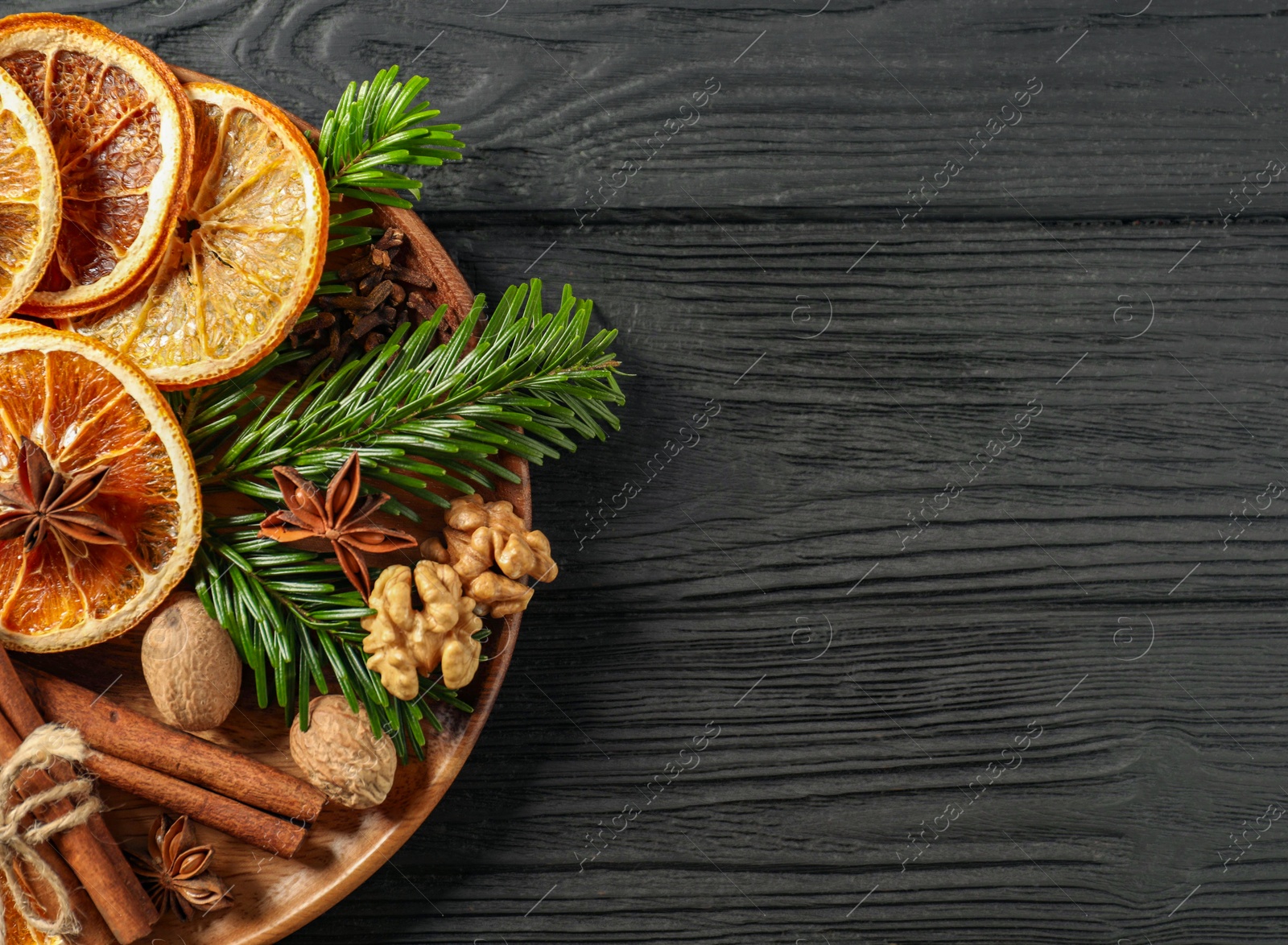 Photo of Different spices, dried orange slices and fir tree branches on black wooden table, top view with space for text. Christmas season