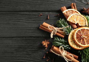 Photo of Different spices, dried orange slices and fir tree branches on black wooden table, flat lay with space for text. Christmas season