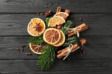 Photo of Different spices, dried orange slices and fir tree branches on black wooden table, flat lay. Christmas season