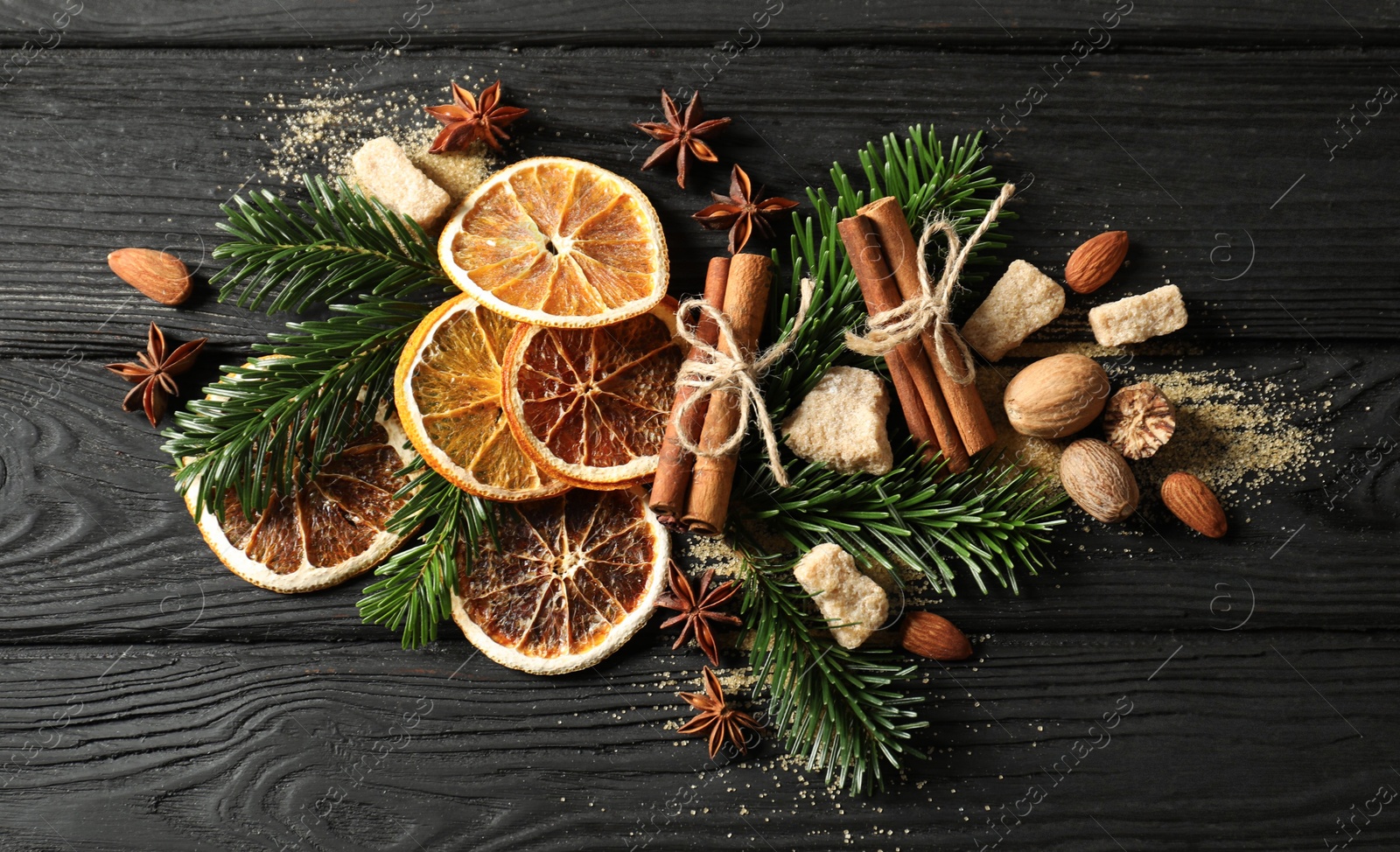 Photo of Different spices, dried orange slices and fir tree branches on black wooden table, flat lay. Christmas season