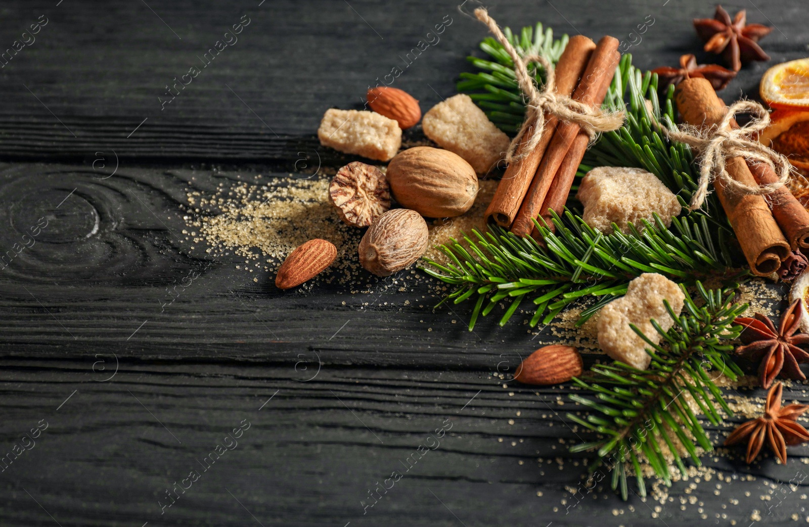 Photo of Different spices, dried orange slices and fir tree branches on black wooden table, closeup with space for text. Christmas season