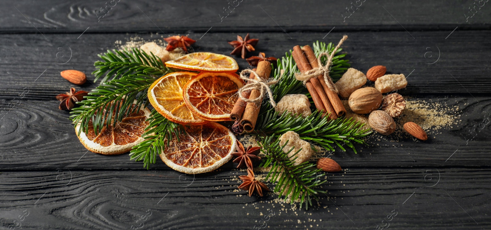 Photo of Different spices, dried orange slices and fir tree branches on black wooden table. Christmas season