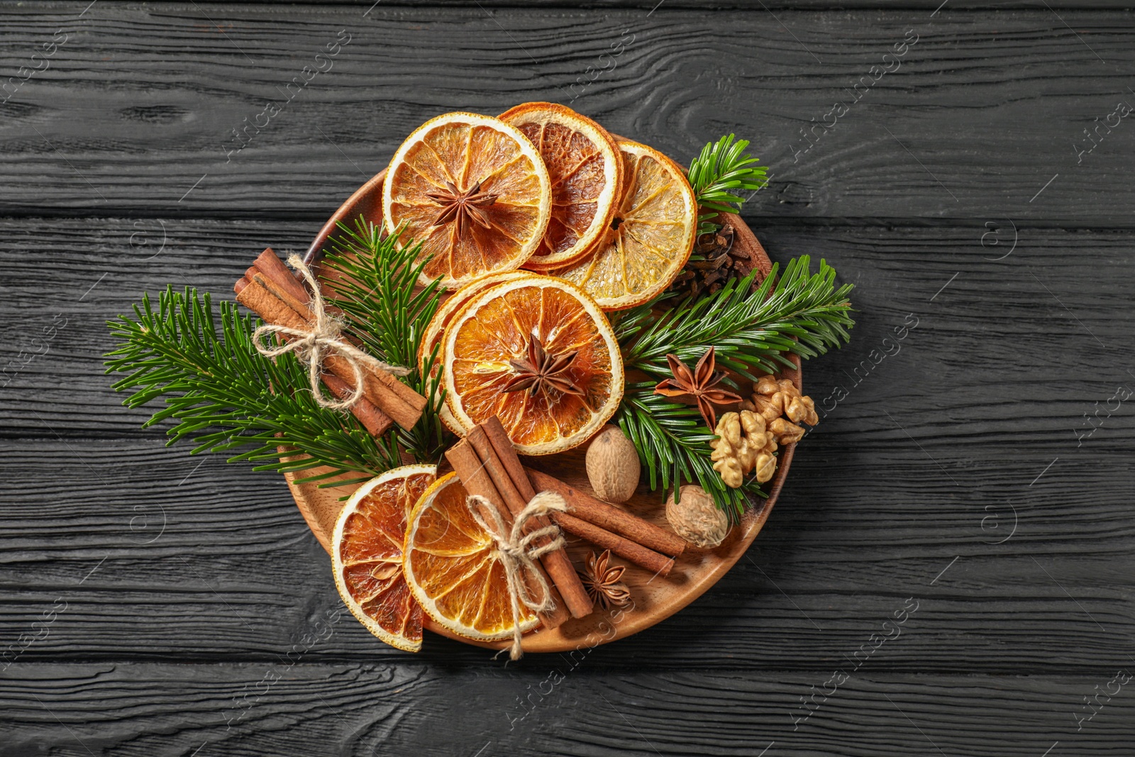 Photo of Different spices, dried orange slices and fir tree branches on black wooden table, top view. Christmas season