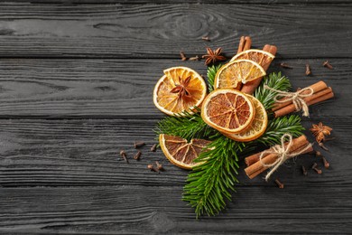 Photo of Different spices, dried orange slices and fir tree branches on black wooden table, flat lay with space for text. Christmas season