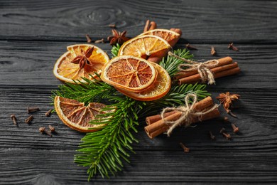 Photo of Different spices, dried orange slices and fir tree branches on black wooden table. Christmas season