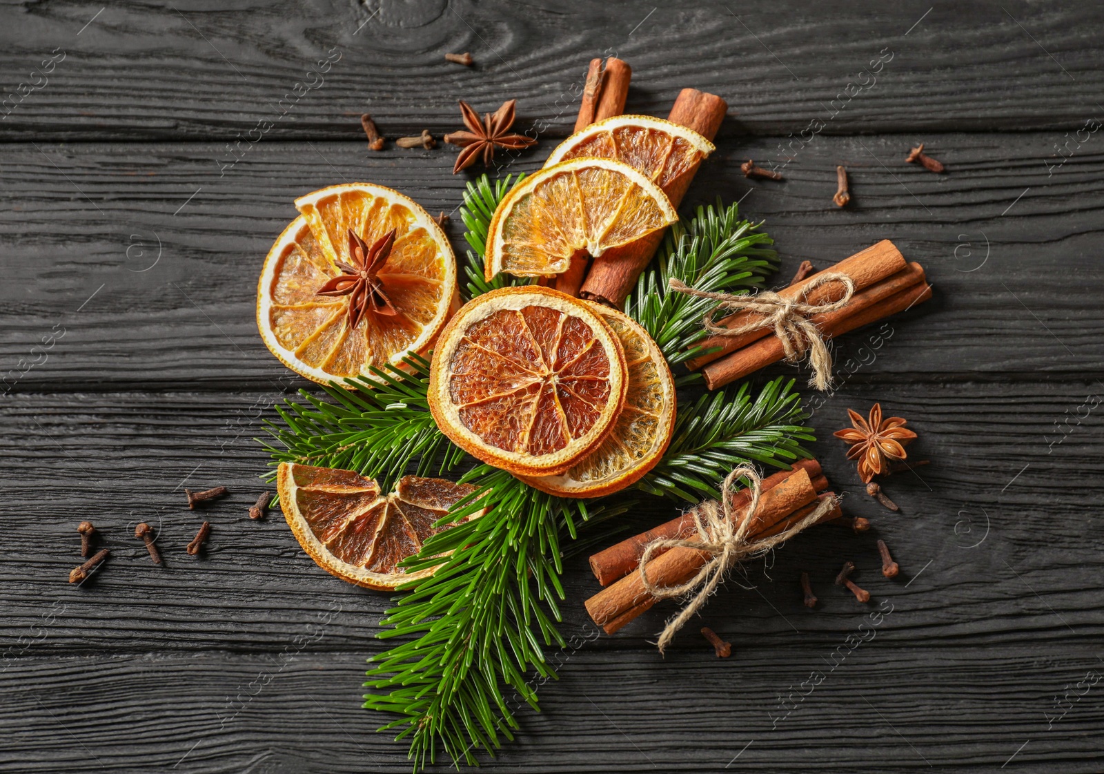 Photo of Different spices, dried orange slices and fir tree branches on black wooden table, flat lay. Christmas season