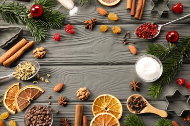 Photo of Frame of different aromatic spices and fir tree branches on grey wooden table, flat lay with space for text. Christmas season