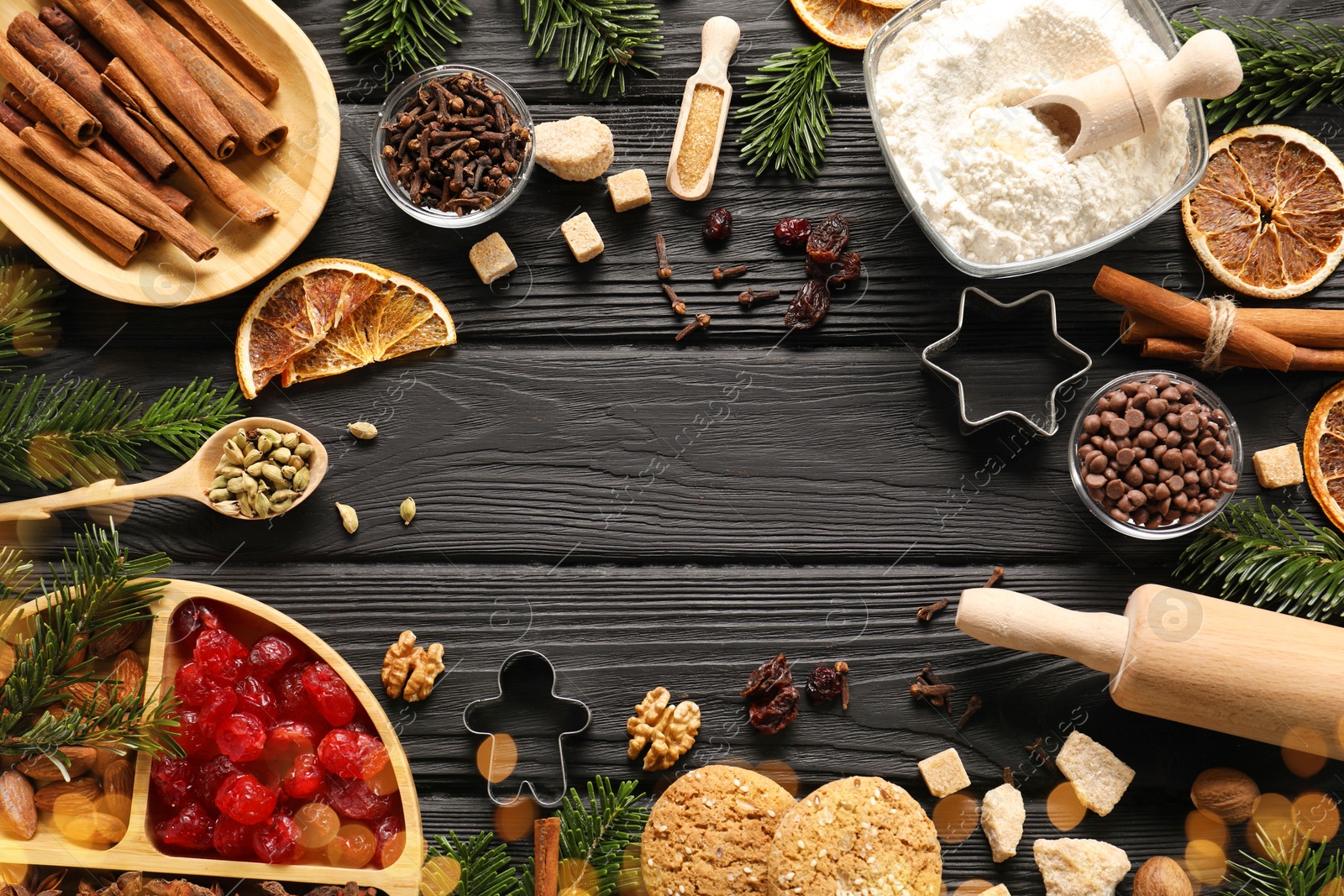 Photo of Frame of different aromatic spices and fir tree branches on black wooden table, flat lay with space for text. Christmas season