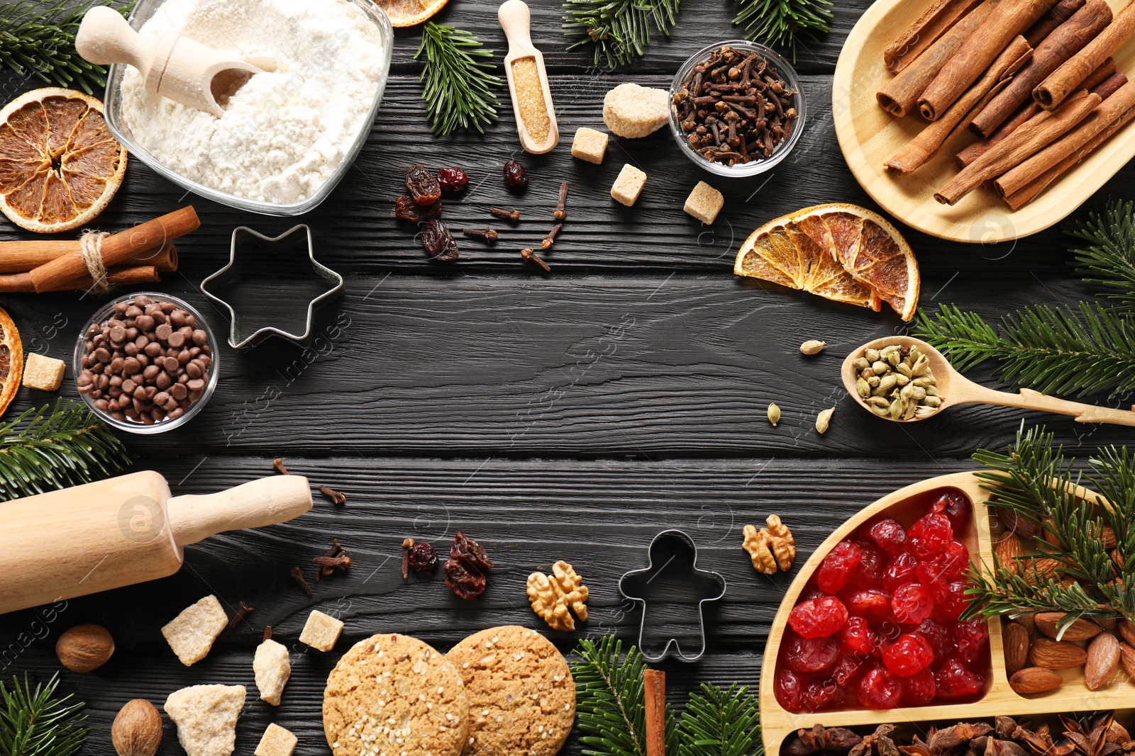 Photo of Frame of different aromatic spices and fir tree branches on black wooden table, flat lay with space for text. Christmas season