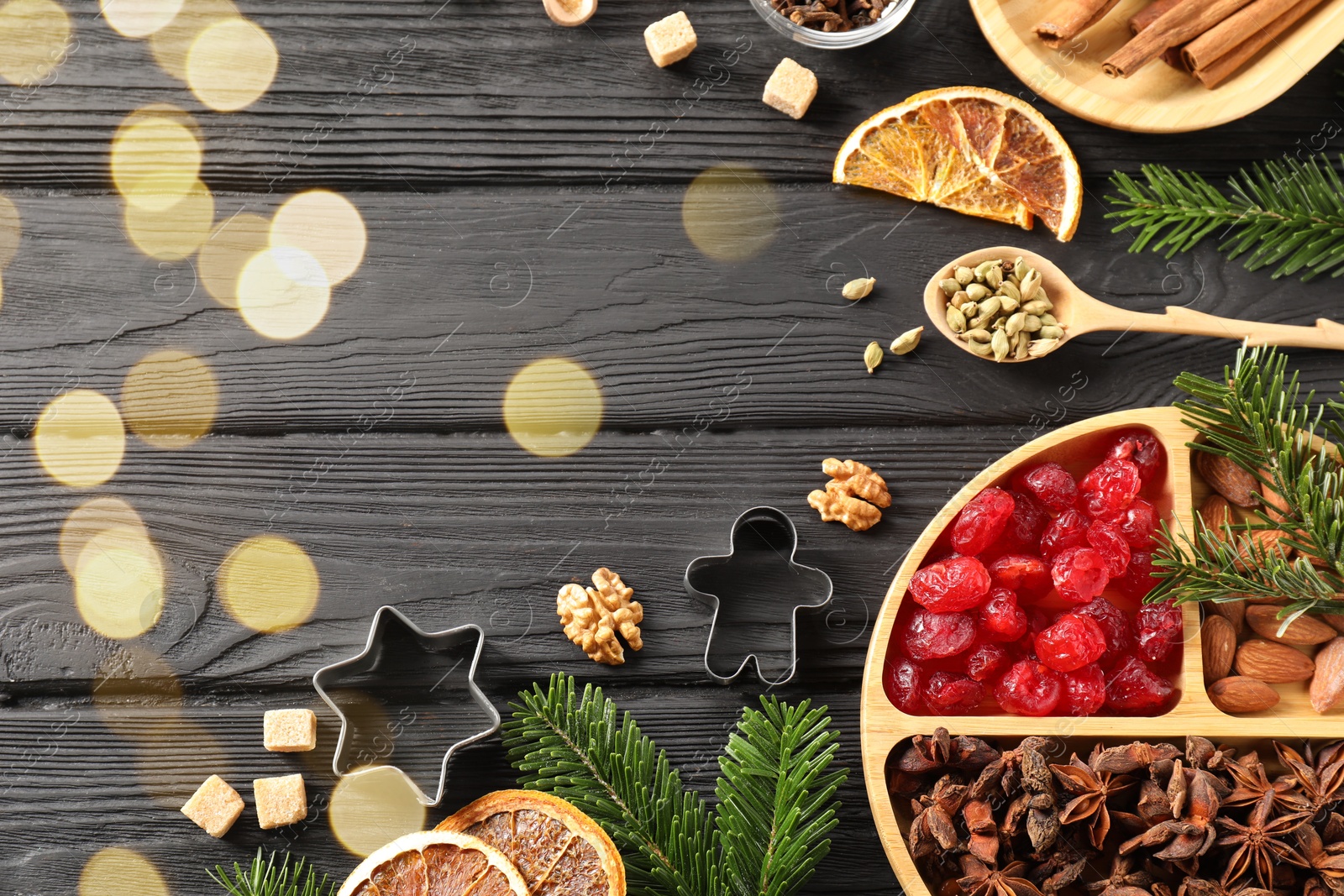 Photo of Different aromatic spices and fir tree branches on black wooden table, flat lay with space for text. Christmas season