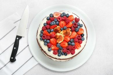 Delicious chocolate sponge cake with berries and knife on light table, top view