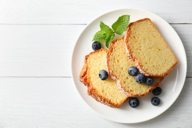 Photo of Freshly baked sponge cake, mint and blueberries on white wooden table, top view