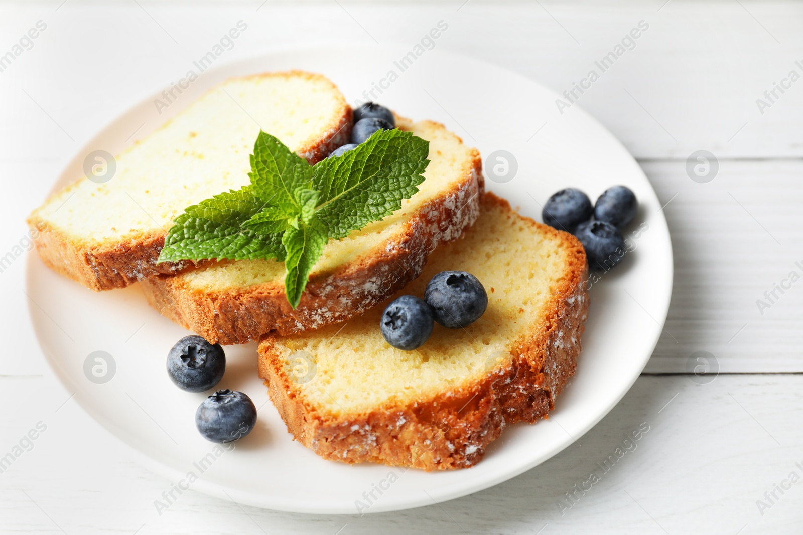 Photo of Freshly baked sponge cake, mint and blueberries on white wooden table, closeup