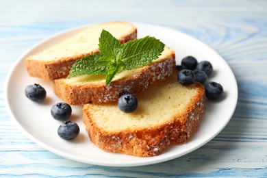 Photo of Freshly baked sponge cake, blueberries and mint on light blue wooden table, closeup