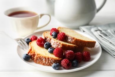 Photo of Freshly baked sponge cake, raspberries and blueberries on white wooden table