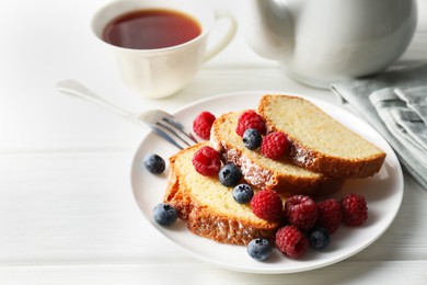 Photo of Freshly baked sponge cake, raspberries and blueberries on white wooden table